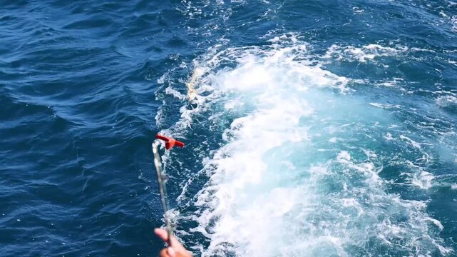 Fisherman holding fishing rod on boat trolling for big game fish in deep blue ocean waters during sunny day.