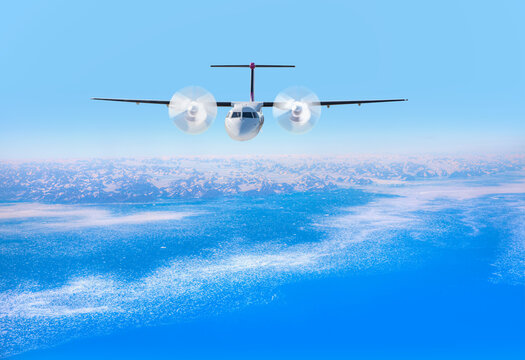 White metallic propeller passenger airplane in the sky - View from airplane of melting polar ice cap and snowy mountains - Greenland