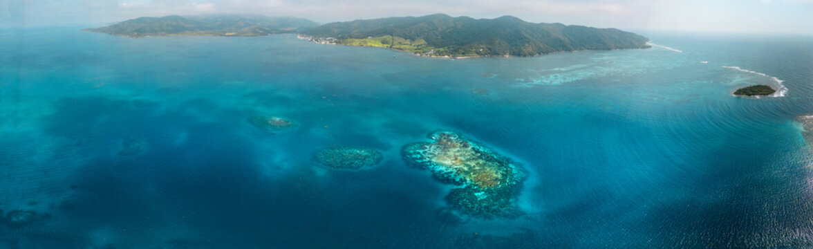 Aerial view of the lush green hills and vibrant coral reefs surrounded by turquoise Caribbean waters of the tropical island landscape in Guanaja, Bay Islands Department, Honduras.