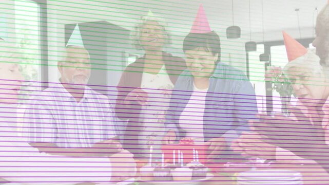 Woman in cone hat placing red box on lit cupcakes by table, guests clapping, marking birthday