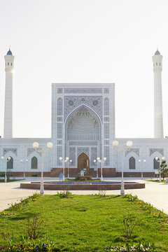 Minor mosque in Tashkent with ornate tilework facade and twin minarets. White Islamic architecture surrounded by green lawns and lampposts, ideal for travel and cultural publications.
