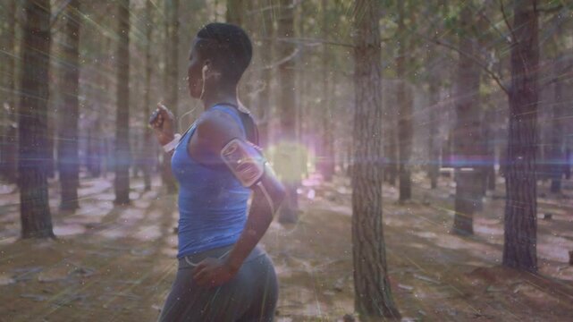 Female runner entering right, jogging forest, phone armband syncing with lens flare for fitness