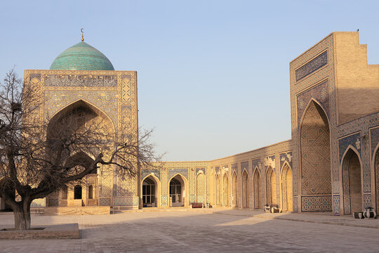 Kalyan Mosque courtyard in Bukhara with turquoise dome and ornate tilework bathed in golden light. Ideal for travel publications, cultural heritage materials, and tourism brochures.