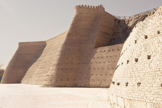 Ark fortress walls in Bukhara with massive sloped brick towers and crenellated parapets. Ancient citadel architecture of Uzbekistan ideal for travel and heritage publications.