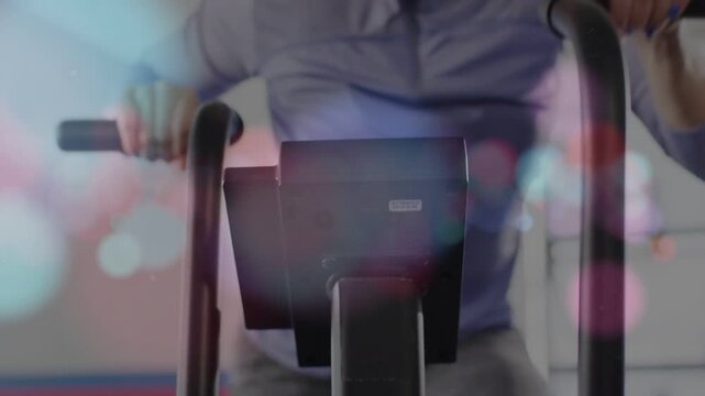 Camera pulling back revealing female fitness rider pedaling fan bike, bokeh overlay softening shot