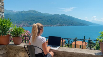 Obraz premium Woman enjoys scenic view while working on her laptop from balcony overlooking beautiful lake and mountains. High quality photo