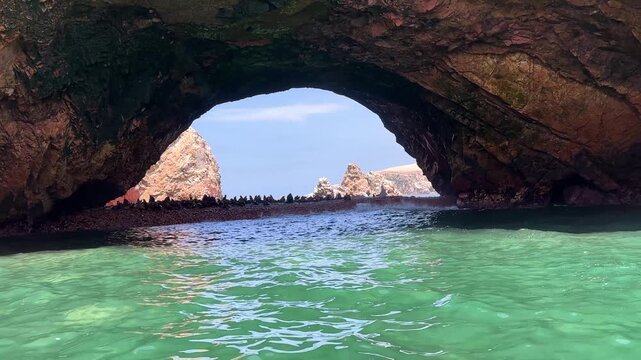 Cinematic view of natural coastal rock arch with South American sea lions resting on rocky platform beneath island formation near Paracas National Reserve, Peru