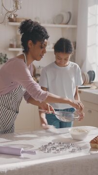 African american mother and her teen daughter cooking together at home kitchen. Happy motherhood and childhood, mom and child sifting flour on table, baking pie or cookies for dessert and dinner