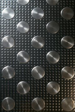 Silver brushed circular studs arranged in regular grid on textured dark metal background industrial geometric pattern for modern industrial design use