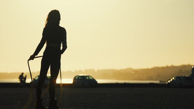 Silhouette of a person dancing with a rope at sunset by the water in a busy location