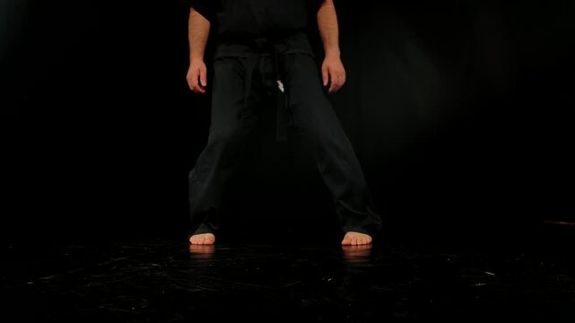 Close up of the legs of a man practicing Wing Chun in a black kimono, demonstrating his skills against a gray studio backdrop, showing self defense training and martial arts techniques.
