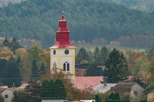Aerial view of the Holy Trinity Church tower with its red roof and clock face surrounded by autumn trees and village houses in the village of Mosovce, Zilina Region, Slovakia.