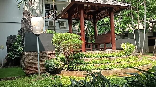 Traditional wooden gazebo in a tropical garden with green plants and stone terrace.