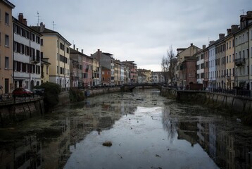 Obraz premium European canal lined with colorful buildings and reflections on a cloudy day