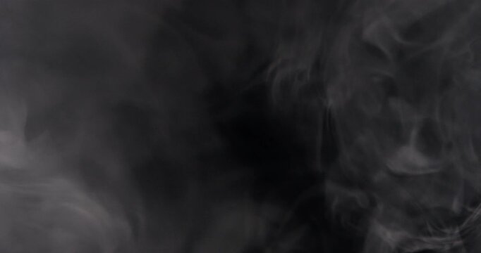 Abstract footage of soft grey smoke swirling and drifting through deep darkness on a black background.