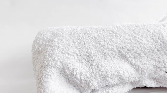 Fresh laundry folded neatly on white table. Woman organizing clean linens at home. Soft towels stacked in tidy pile ready for storage in closet.