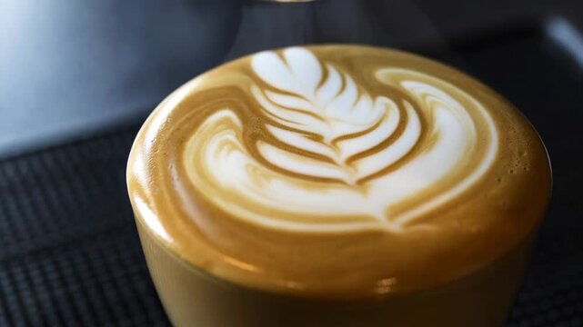 Slow motion close up of milk pour creating latte art pattern on cappuccino in coffee shop counter setting