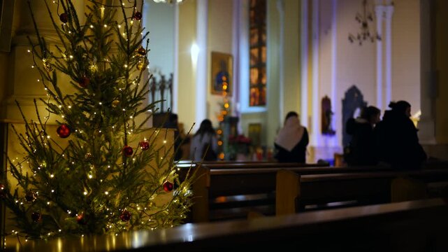 Christmas tree glowing inside a Catholic Church during Advent with parishioners praying