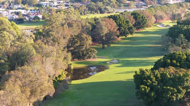 Aerial view of lush green golf course fairway featuring water hazard and bunker during golden hour.