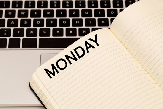 Notebook open to Monday page next to laptop on a desk in a workspace setting during daytime