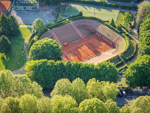 Aerial view of the Circolo della Stampa Sporting tennis stadium with clay court and amphitheater seating surrounded by green trees in Torino, Piemonte, Italy.