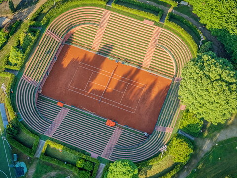 Aerial view of the historic clay tennis court at Circolo della Stampa Sporting with tiered stone seating and lush green hedges in Torino, Piemonte, Italy.