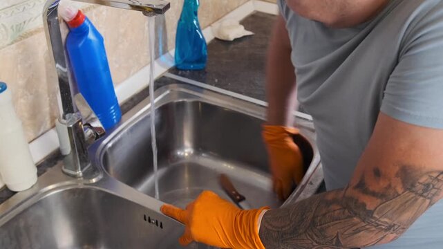 Man scrubbing metal sink with steel wool in close-up side view, removing grease and stains with abrasive sponge under running water, deep cleaning process and kitchen hygiene routine
