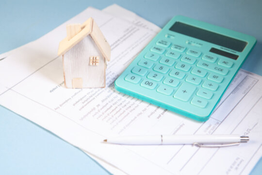 House model, calculator and pen on financial document with blue background.