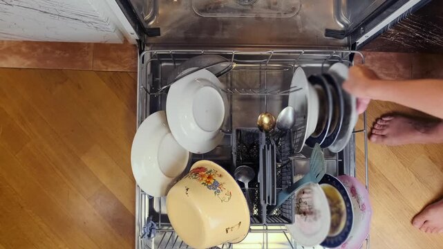 Top view of woman placing dirty plates and utensils into dishwasher, household cleaning routine in modern kitchen, daily chores, hygiene and domestic life concept