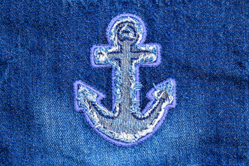 Close up of a denim fabric with an anchor patch sewn into the material showing details of stitching and texture © Fleuronica