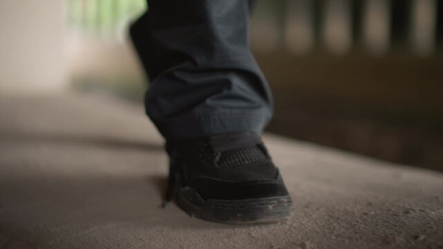 Closeup of wet sneaker stepping on concrete, slowmotion raindrops splashing, reflective puddle shimmer underpass glow, denim cuff brushing gritty surface, commuter stride conveying determination