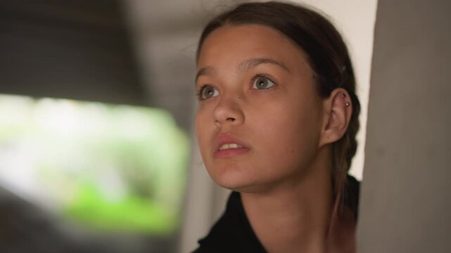 Multiracial teen peeks around concrete pillar, curious in underpass. Closeup sequence of a young multiracial girl scanning shadowy tunnel, soft bokeh background, subtle smiles and cautious glances