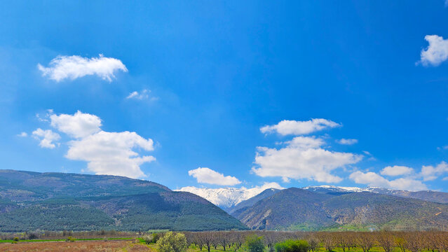 A dramatic seasonal landscape of the Sultandağları mountains between Afyonkarahisar and Konya, where snow-covered peaks rise above valley orchards of Akşehir-&Ccedil;ay cherry trees blooming in white