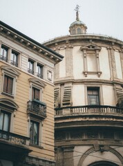 Obraz premium Title / Description: Classic Milanese architecture: Detailed view of a traditional residential building next to a historic domed structure in Milan, Italy. Elegant facades with wrought-iron balconies 