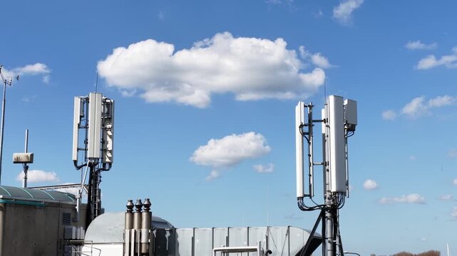 Telecommunication cell tower antennas on rooftop with moving clouds