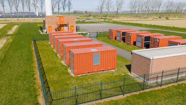 Aerial view of a battery energy storage system with orange containers and a wind turbine base near a solar farm in Middelharnis, Zuid-Holland, Netherlands.
