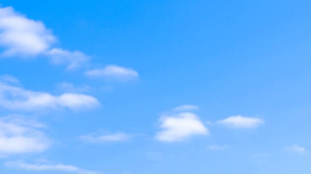 Time lapse pan of clouds drifting across clear blue sky in wide panoramic daytime view of soft white cumulus formations