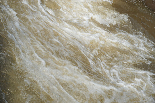 The texture of the river water flow is fast, murky and has white foam in the rapids area.