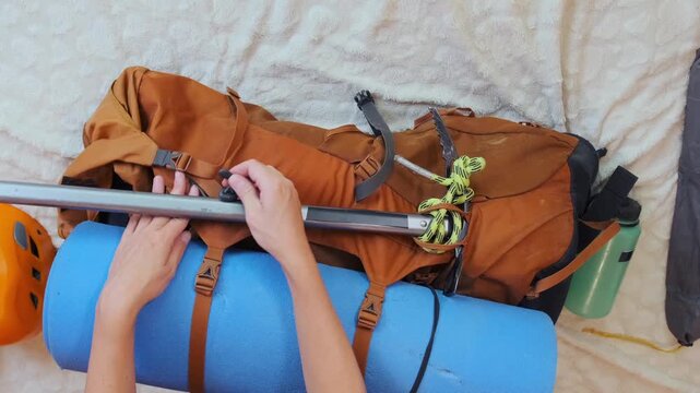 Overhead view of woman securing ice axe to hiking backpack, preparing technical mountaineering equipment for alpine climb, organizing gear for mountain expedition and extreme outdoor adventure