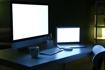 Fototapeta premium Modern programmer's workplace with computer monitor, laptop and cup of tea in office at night, closeup