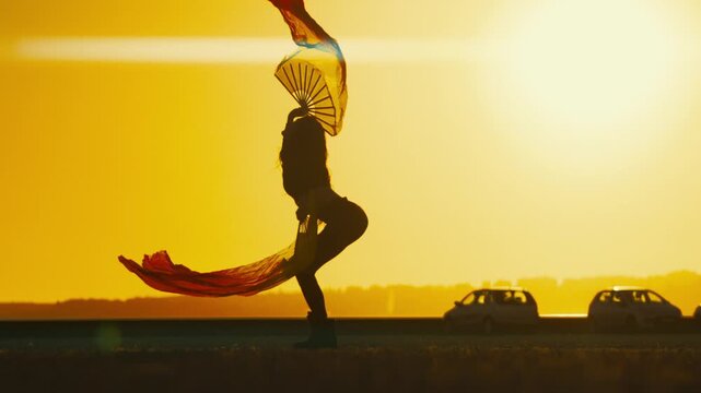 Dancer twirls colorful fans during sunset by the road in city