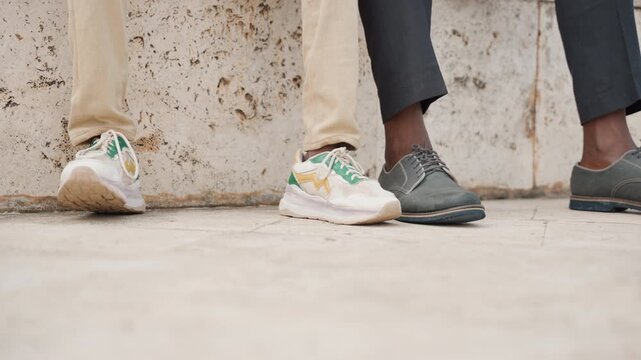 Closeup father and son shoes against concrete wall, casual sneaker and leather shoe, cropped legs and pavement foreground, quiet urban bond, subtle contrast in style, warm afternoon light
