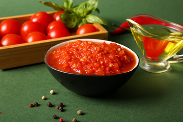 Naklejka premium Bowl of tasty tomato sauce and ingredients on green background, closeup