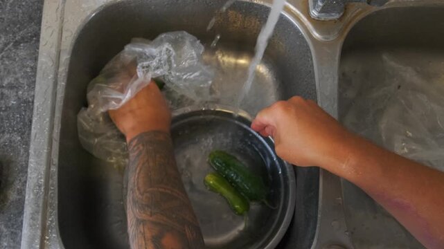 male hands washing cucumbers top view rinsing fresh vegetables under running water in kitchen sink, cleaning ingredients for cooking meal, home food prep and hygiene process