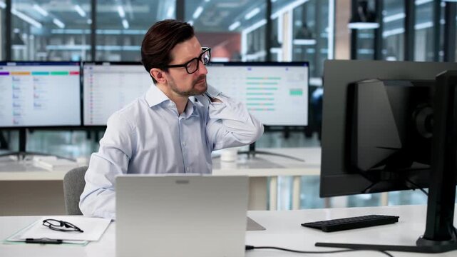 Man Sits At Office Desk Rubbing Neck To Relieve Pain