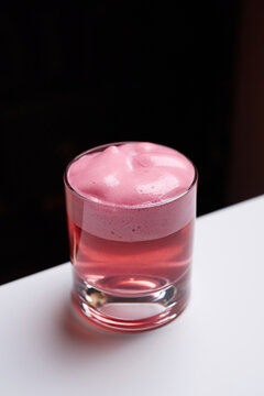 Close-up of a pink cocktail with thick foam in a rocks glass on a white table