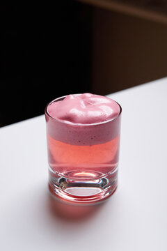 Close-up of a pink cocktail with thick foam in a rocks glass on a white table