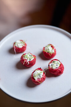 Close-up of elegant red choux pastry appetizers filled with white mousse, garnished with sprouts and sesame on a white plate. Gourmet catering, buffet, banquet, or wedding reception scene