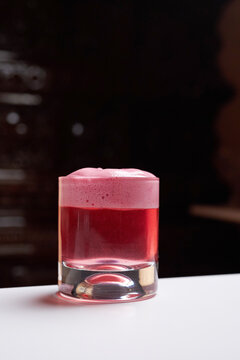 Close-up of a pink cocktail with thick foam in a rocks glass on a white table