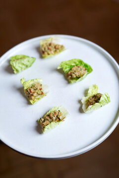 Fresh lettuce leaf appetizers with gourmet filling served on a white round plate. Elegant healthy catering, banquet appetizers, or fine dining buffet scene